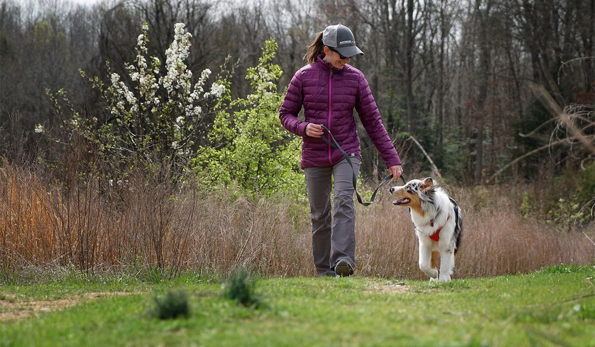 Maria walking her dog through grass by woods.