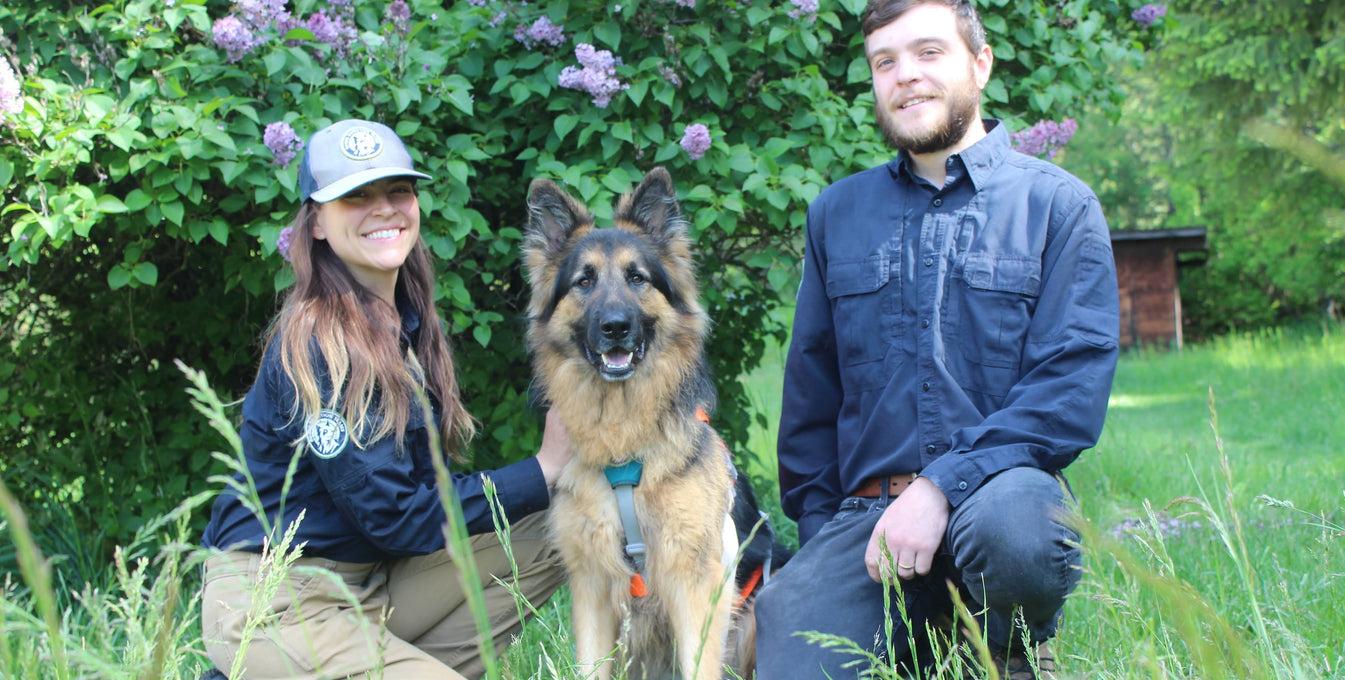 Hugo, a Rogue Detection Dog, poses with his two family members.