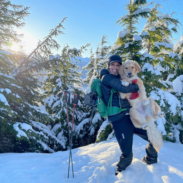 A woman picks up her golden retriever dog and poses with him in the snow. 