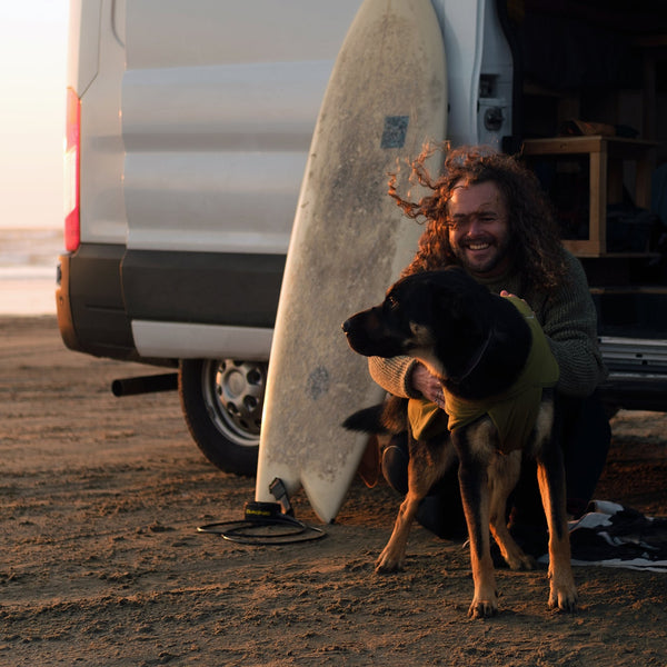 A man sits behind his truck with his dog on a bed