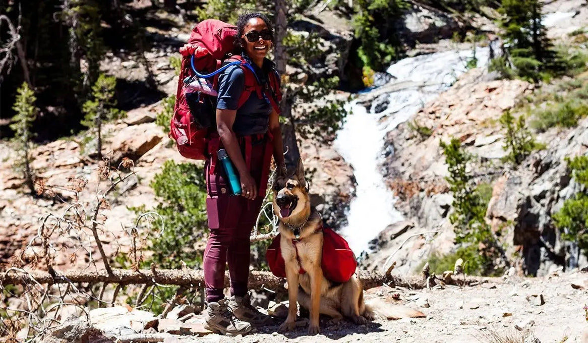 Noami and Amari with backpacks on stand in front of an alpine waterfall.